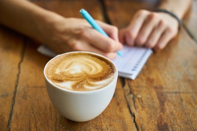 A person writing on a notebook next to a cup of coffee in their Fayetteville apartment.