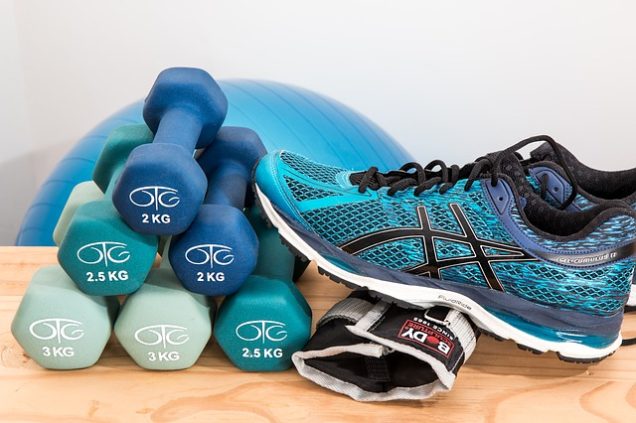 A pair of ASICS shoes and a pair of dumbbells are placed on a wooden table in an apartment in Fayetteville, NC.