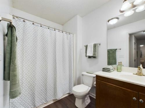 Apartments in Fayetteville, North Carolina A clean bathroom with a shower curtain, toilet, vanity, and mirror. Towels are neatly hung on the wall and placed on the counter. The room is well-lit with overhead lighting.