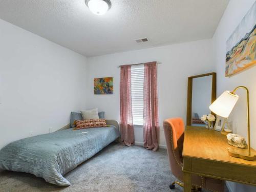 Apartments in Fayetteville, North Carolina A small bedroom featuring a single bed with gray bedding, a wooden desk with a pink chair, and abstract art on the walls. A window with curtains allows natural light to enter the room.